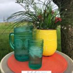 A Pinterest pin with a picture of a glass half full sitting by a water pitcher and vase of flowers. Designed for this post about keeping a positive perspective.