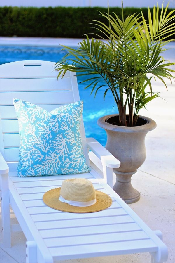 A picture of a pillow and sun hat sitting on a chaise lounge by a pool for this post about the benefits of self-care.