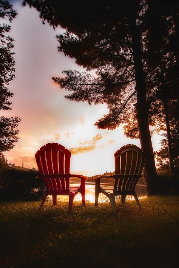 A picture of two empty chairs facing a lake at sunset for this post about waiting with patience on God's timing.
