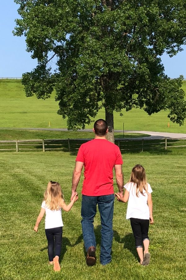 A picture of my husband walking hand in hand through an open field with our two daughters for this post about dads and their daughters.