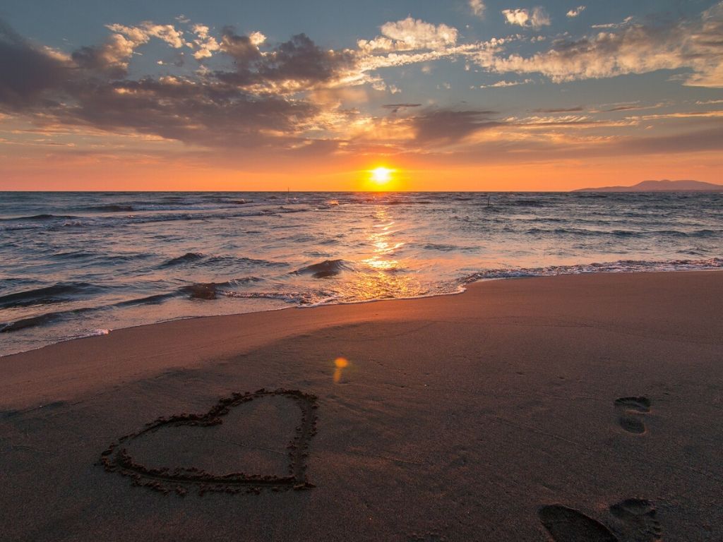 A picture of a heart drawn in the sand at sunset for this post about investing in marriage by getting away together.