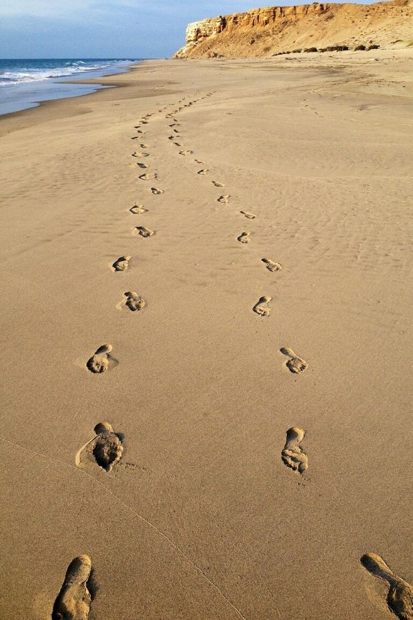 A picture of a pair of footprints in the sand for this post of romantic getaway tips for parents on a budget.