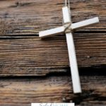 A Pinterest pin with a picture of a white cross on a wooden background. Designed for this post about overcoming fear with faith.