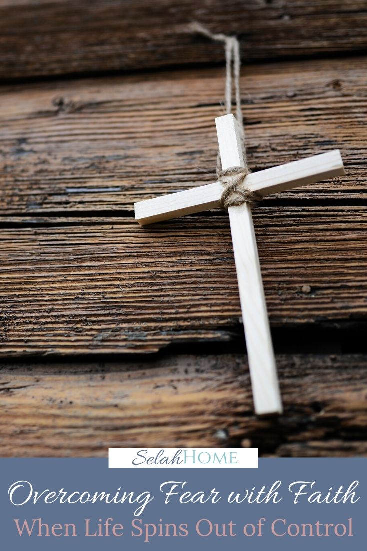 A Pinterest pin with a picture of a white cross on a wooden background. Designed for this post about overcoming fear with faith.
