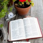 A Pinterest pin with a picture of a flower pot and clock beside an open Bible. Designed for this post about the power of faith in God.