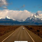 A Pinterest pin with a picture of a car on the highway driving toward the mountains. Designed for this post full of tips on family road trip essentials.