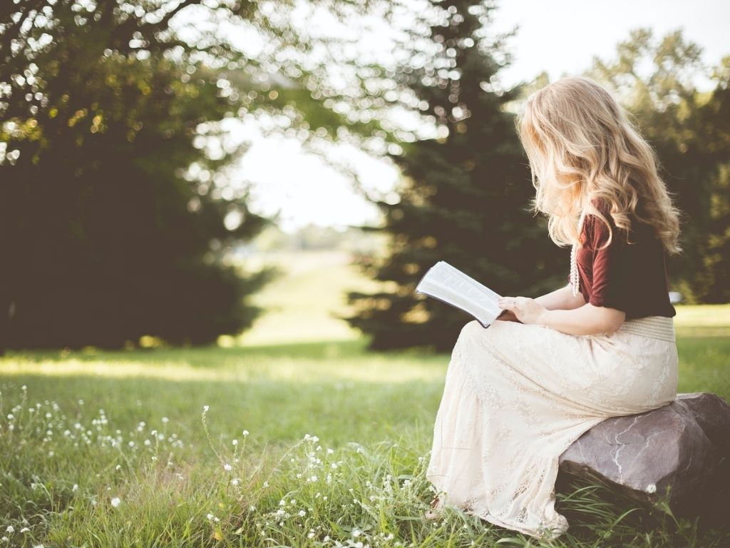 A picture of a woman reading in a sunlit field for this post on how to be a more patient mom.