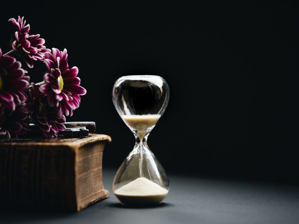 A picture of an hourglass, flowers, and book for this post about what to do while waiting on God.