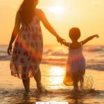 A Pinterest pin with a picture of a mother and daughter walking on the beach. Designed for this post about finding joy in motherhood.