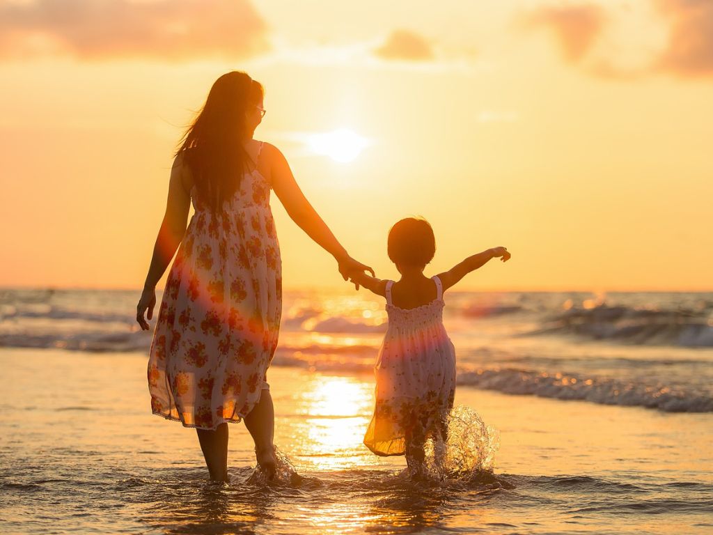 A picture of a mom and daughter walking on the beach for this post about finding joy in motherhood.