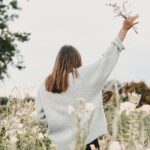 A picture of a woman in a field of flowers raising her hand in worship for this post about choosing faith over feelings.