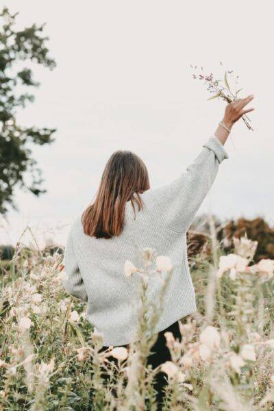 A picture of a woman in a field of flowers raising her hand in worship for this post about choosing faith over feelings.