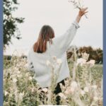 A Pinterest pin with a picture of a woman in a field of flowers raising her hand in worship. Designed for this post about choosing faith over feelings.