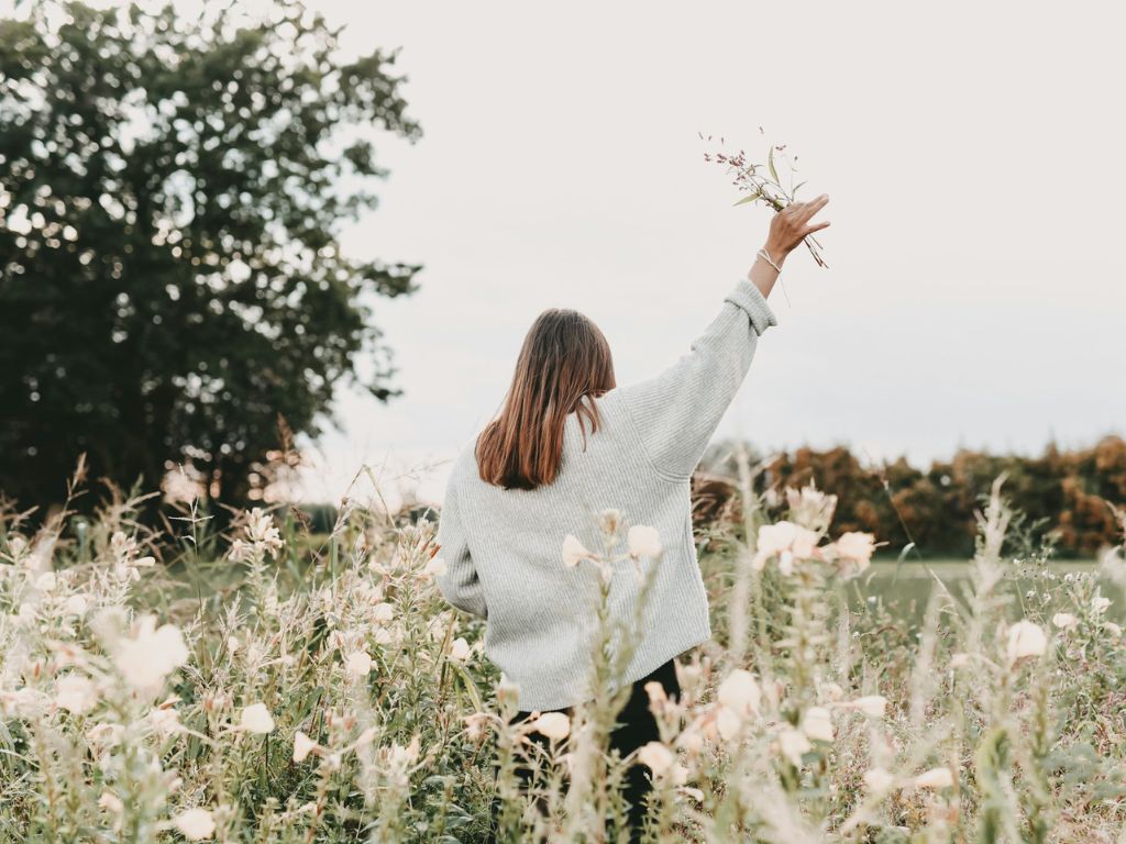 A picture of a woman in a field of flowers raising her hand in worship for this post about choosing faith over feelings.