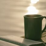 A picture of a Bible and coffee cup sitting by the water for this post of bible verses for anxiety and fear.